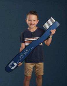 Boy holding giant toothbrush with “Selle Family Dental” logo